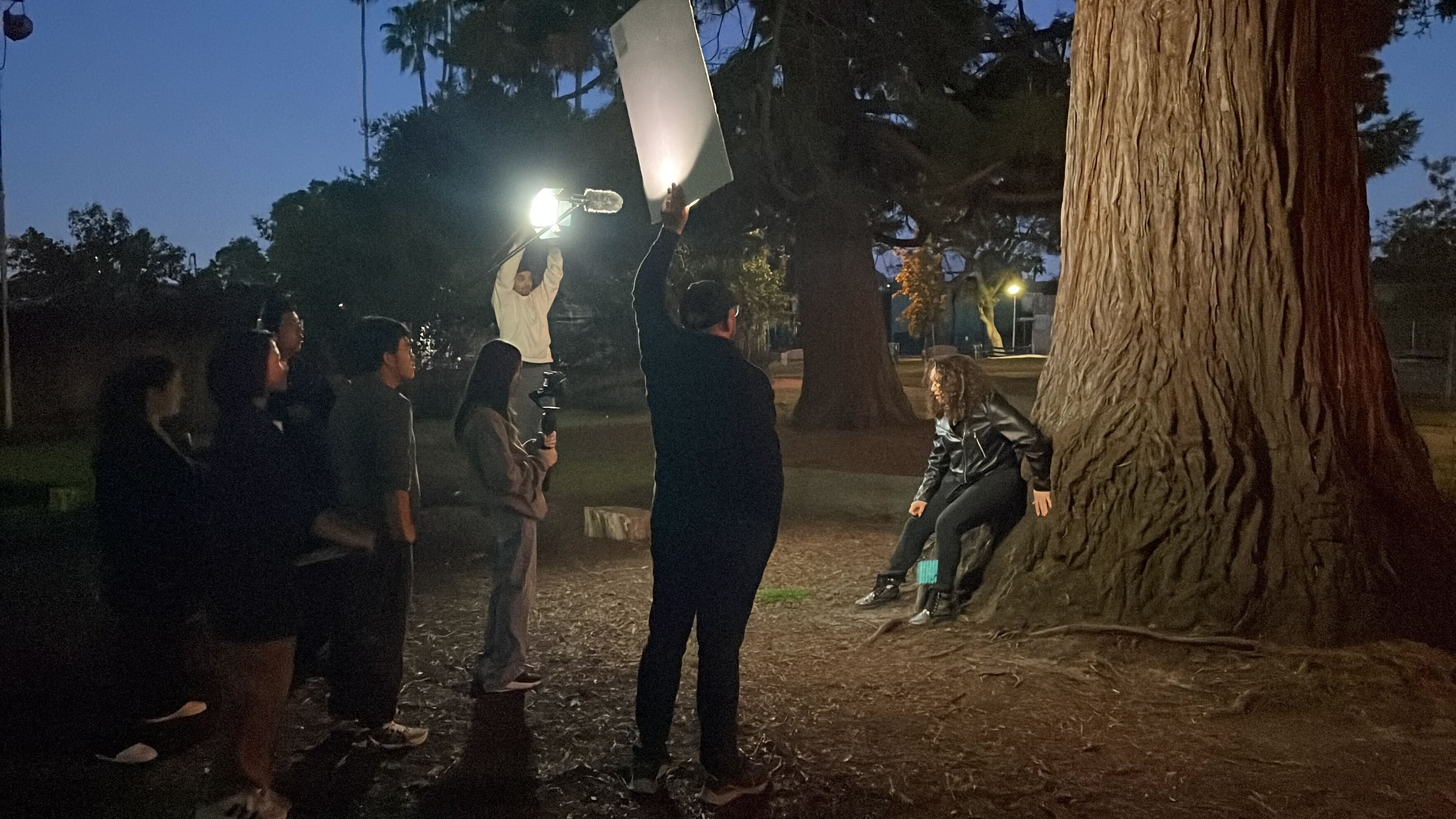 REEL students lighting a night scene on set under a large tree